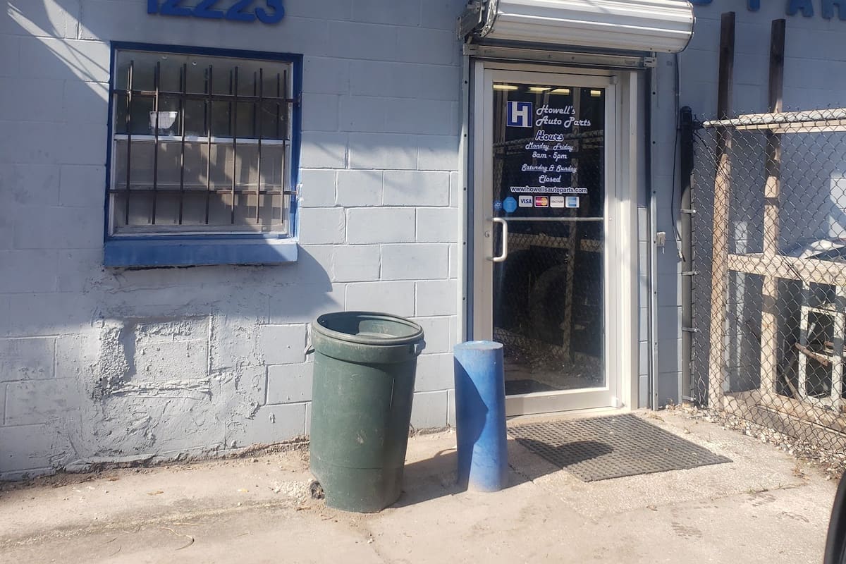 Howell's Used Cars & Auto Parts: Blue-lettered cinder block building with a glass entrance door, barred window and chain-link fence beside it