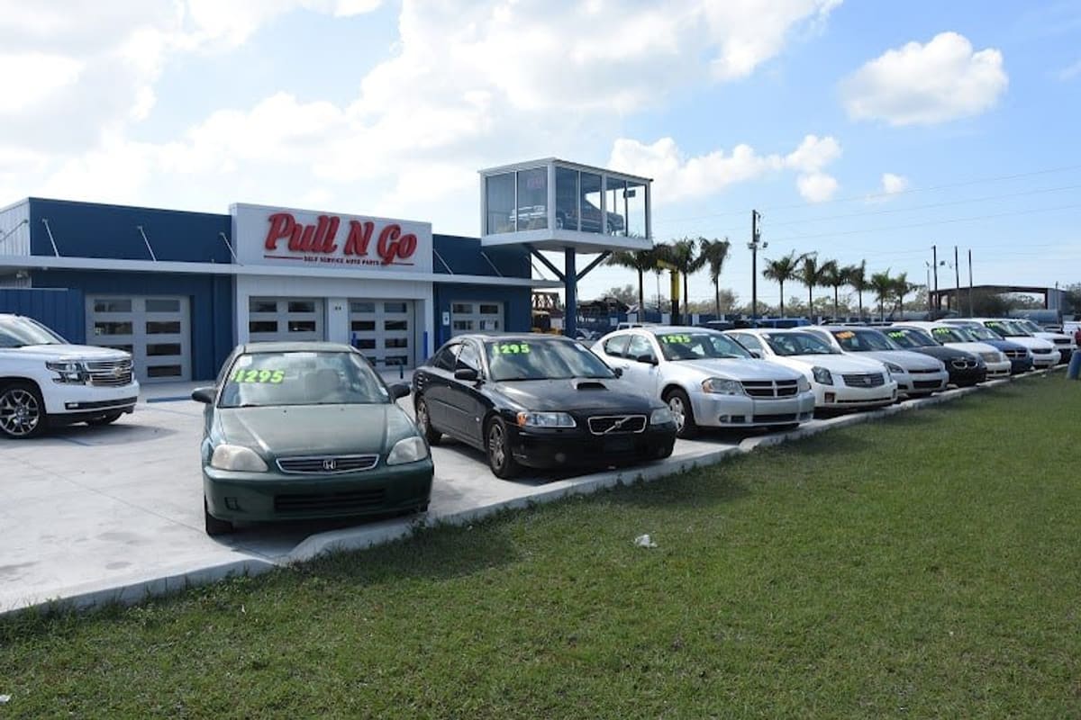 Pull N Go Self Service Auto Parts: Blue and white auto parts building with a red sign, cars parked in rows in front and a grassy strip along the lot