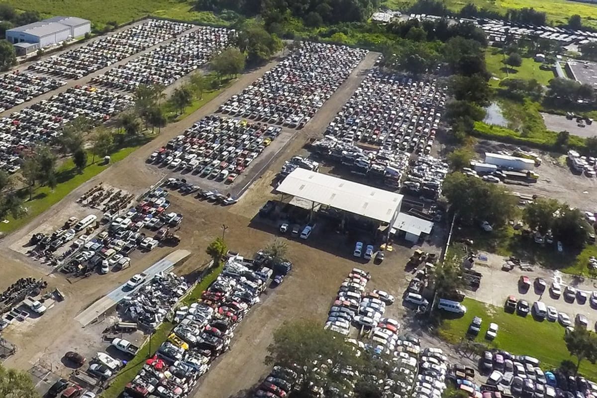 Budget U Pull It of Orlando: Aerial view of a large salvage yard with long rows of cars, a covered work area, and small buildings surrounded by trees