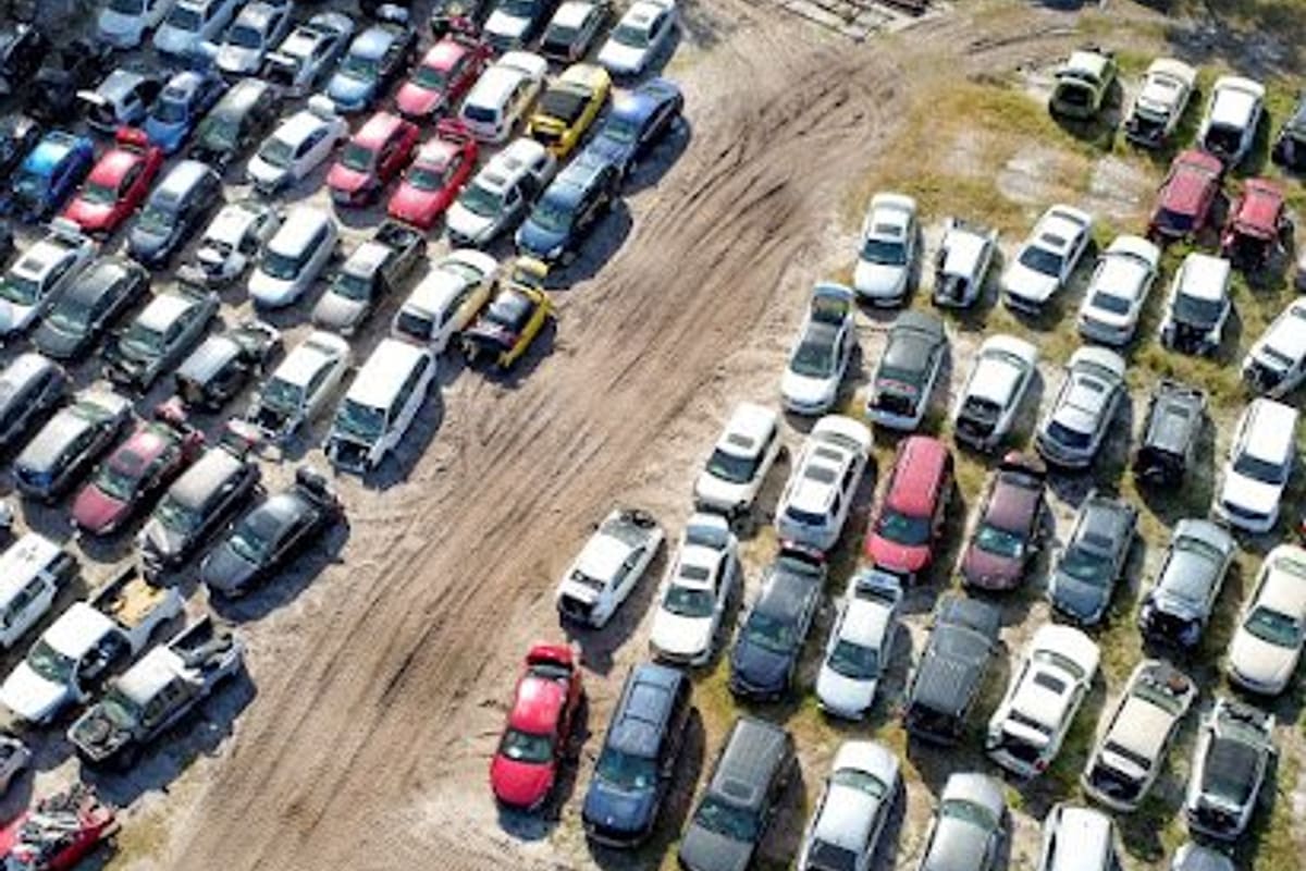 Raw Auto Parts: Aerial view of a salvage yard with rows of cars parked on dirt and grass on either side of a dirt track