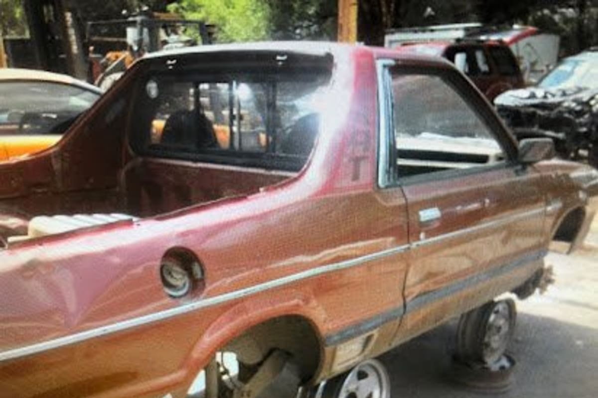 A B C Used Parts: Stripped red pickup resting on stands in a salvage yard with other wrecked vehicles parked behind it