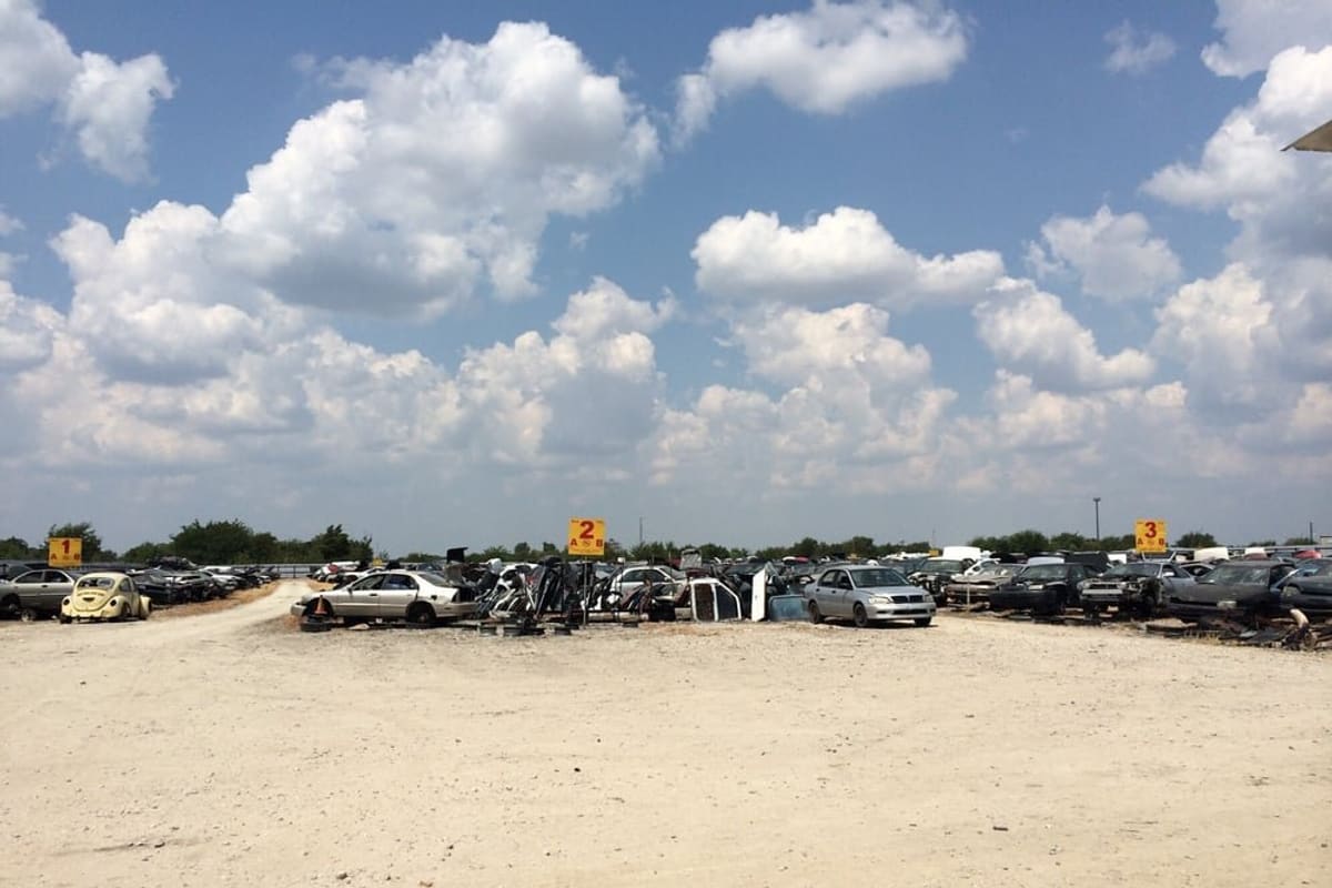 Meribe Motors Auto Salvage: Wide view of a dirt salvage yard with rows of wrecked cars under a blue sky with clouds and numbered row signs