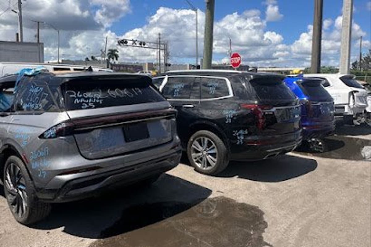 All Parts International: Damaged SUVs with chalk markings parked in rows on a paved salvage lot under a partly cloudy sky
