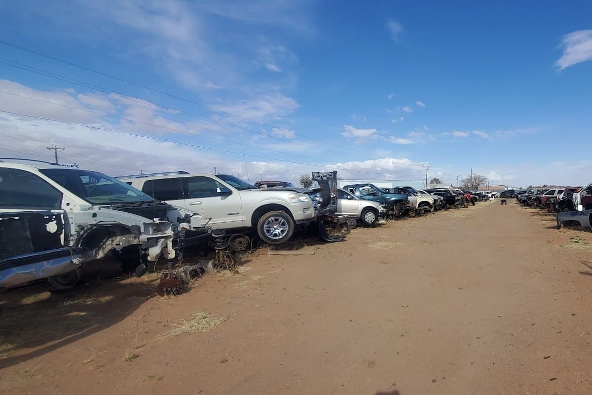 Dyer Auto Salvage: Wide view of a dirt lane lined with rows of salvage cars and trucks under a blue sky with scattered clouds
