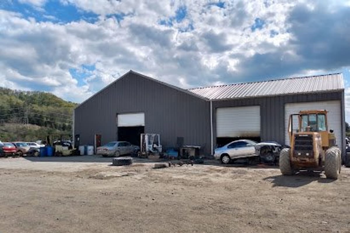 Tri-City Auto Parts: Large gray metal shop building with open bay doors, cars and a yellow loader parked on a dirt lot