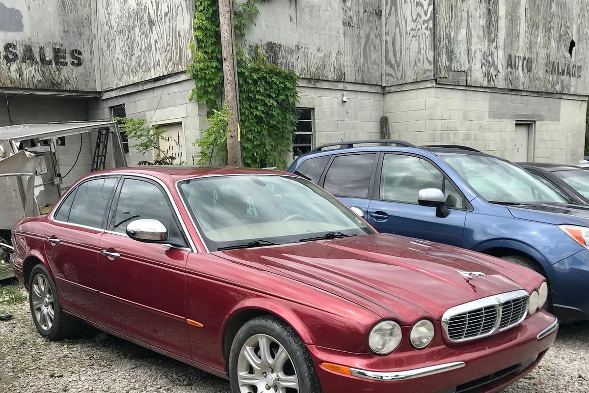 All Things Automotive: Gravel lot with parked cars in front of a weathered concrete and plywood building marked auto salvage