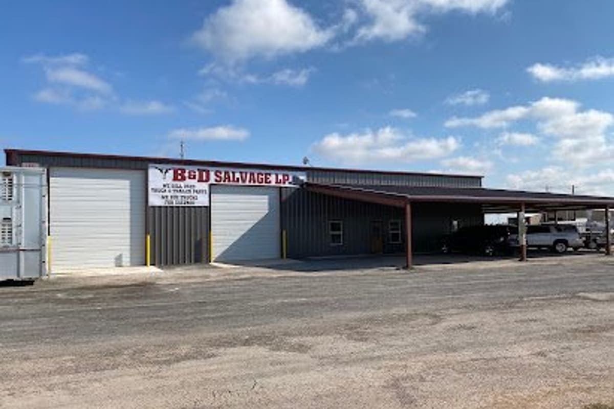 B&D Salvage: Metal shop building with two roll-up doors, a sign above, and a covered parking area under a blue sky