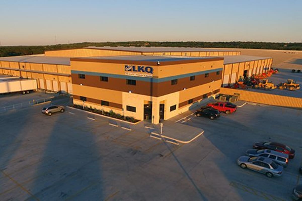 LKQ Central Texas - Goodwin: Aerial view of a large salvage facility with office building, loading docks, parking lot, and equipment at sunset