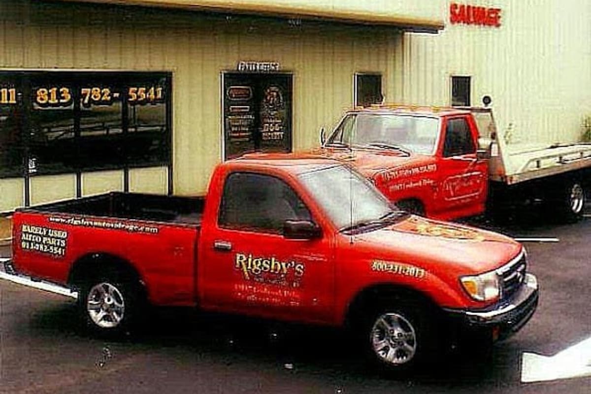 Rigsby's Auto Parts & Sales: Cream metal warehouse building with red lettering and two red pickup trucks parked in front
