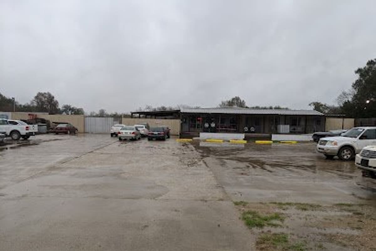 4 Star All Foreign Parts: Wide view of a gravel and concrete lot with parked cars and a low single-story building under an overcast sky