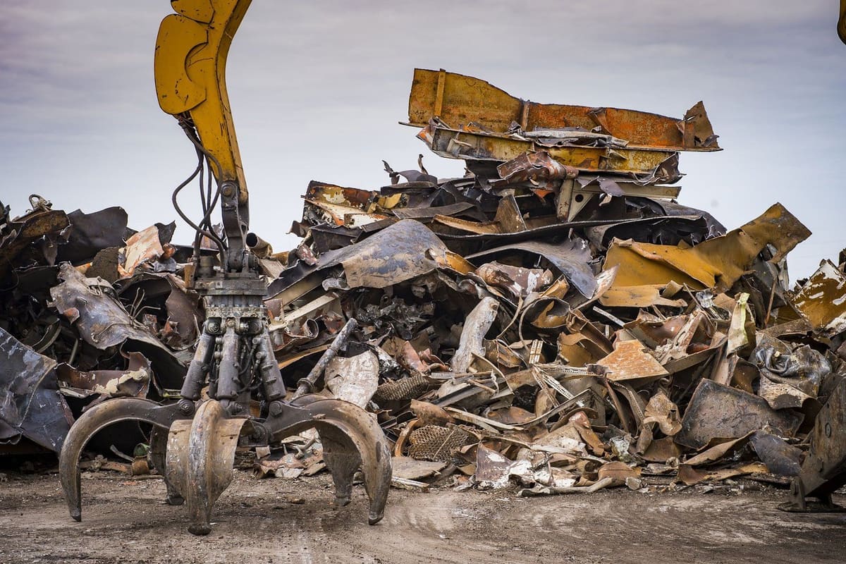 Mark's Metal Recycling: Scrap metal grapple excavator beside a large pile of crushed and rusted metal in an outdoor recycling yard