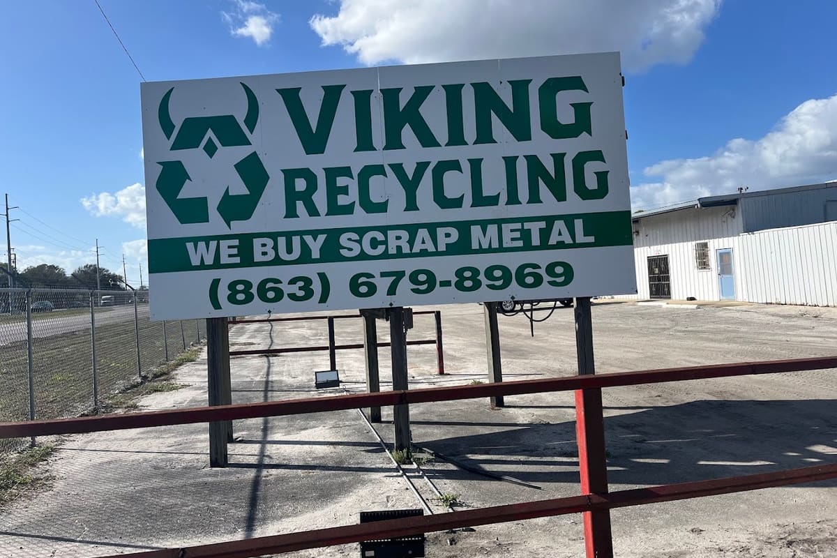 Viking Recycling: Large green and white scrap metal recycling sign with phone number in front of an open gravel lot and white metal building