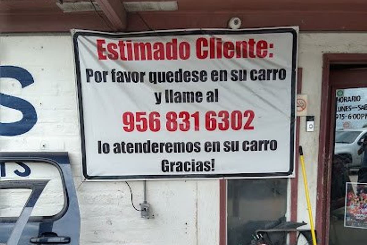 Heles Used Auto Parts: Covered storefront entrance with a Spanish customer notice banner and a pile of used auto parts beside the door
