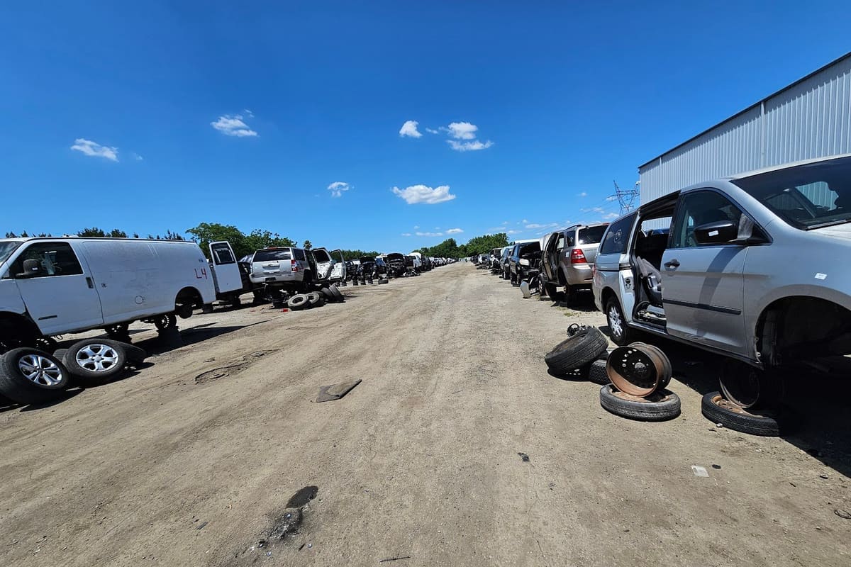 Pick Your Part - Orlando: Wide daytime view of a dirt lane lined with rows of salvage vehicles and loose tires under a blue sky