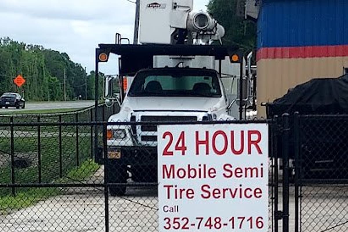 Wildwood Auto Repair & Wrecker Service: Chain-link gate with a sign for 24 hour mobile semi tire service and a white bucket truck parked behind it