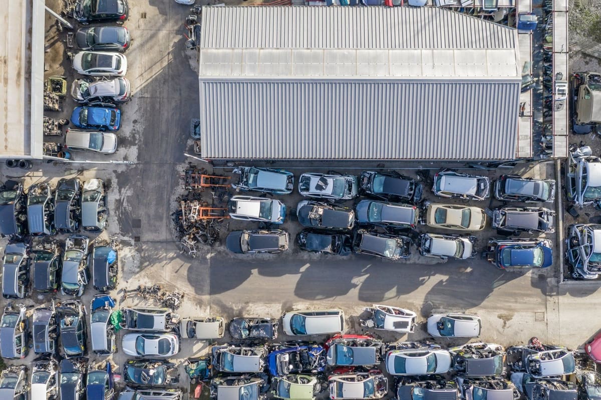 City Salvage: Aerial view of a salvage yard with rows of vehicles parked around a large metal-roofed warehouse building