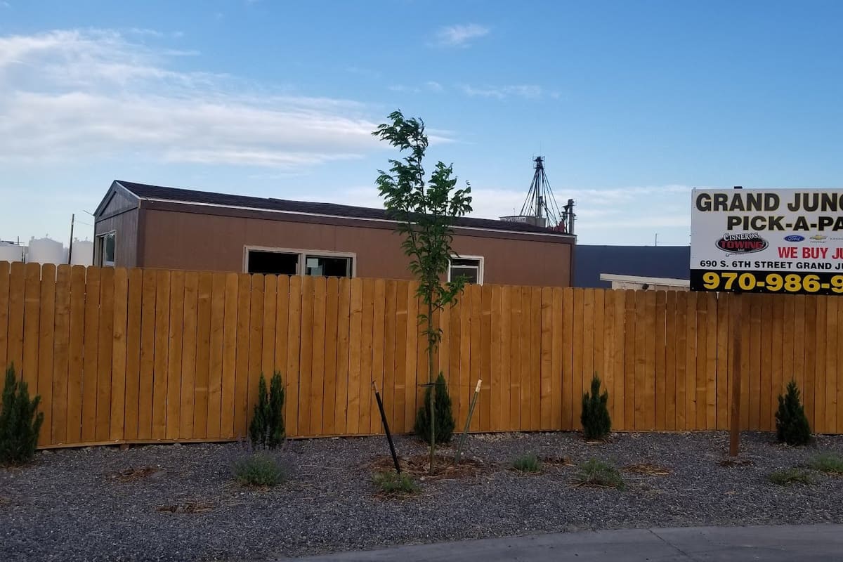 Grand Junction Pick-A-Part: Business sign with phone number above a new wooden fence and gravel landscaping, with a small office building behind